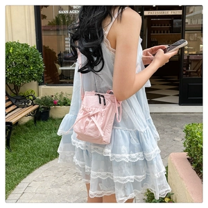 Pink crossbody bag with a bow detail and pleated pocket shown on a model outdoors