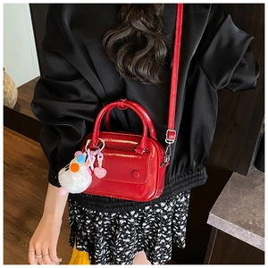 Detail of red patent leather pillow bag with fluffy pom-pom charm and round buckle