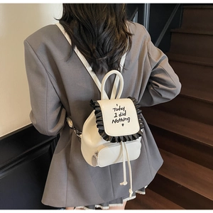 Detail of white mini backpack with black ruffle trim and handwritten slogan for students