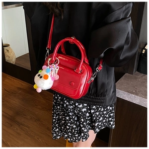 Detail of a bright red glossy hand bag with a cute white pom-pom charm and heart tag