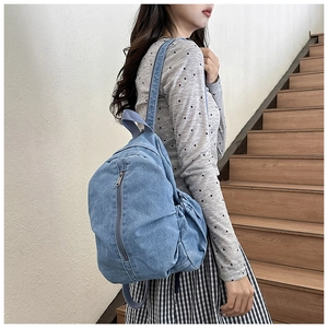 Sac à dos en denim bleu porté sur l'épaule avec poche avant zippée et design minimaliste