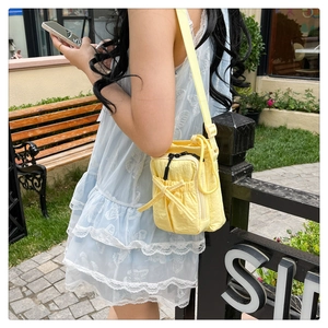 Outdoor shot of a pale yellow mini nylon crossbody bag with bow detail on a model
