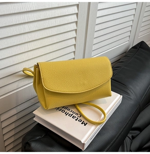 Détail du sac à bandoulière en cuir jaune grainé sur un livre blanc, style minimaliste