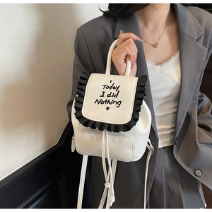 Close-up of a white mini backpack with black lace trim and printed artistic lettering
