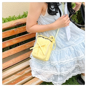 Detailed view of yellow crossbody bag with bow decoration worn by model on park bench