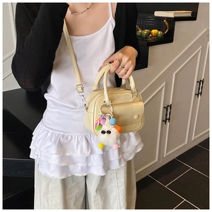Close-up of cream yellow PU leather handbag with white plush charm and shoulder strap