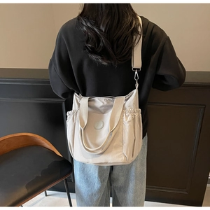 Detail of light grey large nylon tote bag with side pockets and adjustable strap shown on model