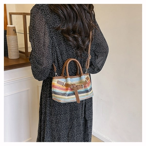 Detail of colorful woven straw tote with leather handles worn by a model in a cafe setting