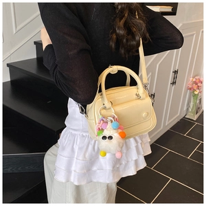 Detail of cream white faux leather pillow bag featuring a plush monster charm and strap