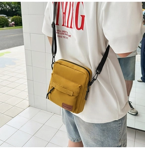 Outdoor street shot of a yellow canvas crossbody phone bag with adjustable black strap