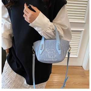 Light blue denim tote bag detail featuring white dog embroidery and golden hardware accents
