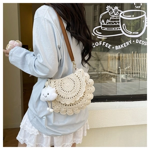 Detail of crochet straw shoulder bag with lace edges and a white cloud charm