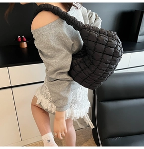 Detailed side view of a black quilted cloud bag with puffy texture and wide shoulder strap