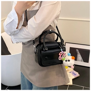 Close-up of black glossy pillow bag with thin strap and a colorful monster charm detail