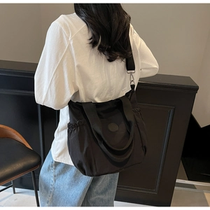 Model wearing a large black canvas crossbody bag with adjustable strap and side pockets