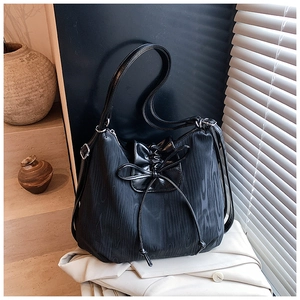 Detail of black textured tote bag with leather bow drawstring on a white fabric background