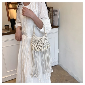 Detail of white bohemian woven bag with cotton tassels and light wooden beads