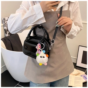 Close-up of black glossy mini pillow bag featuring a cute white plush monster charm