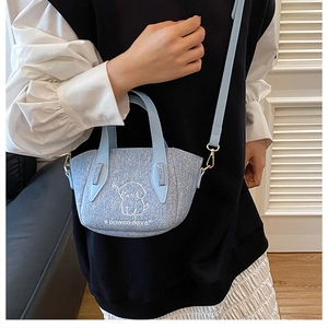 Detail of light blue denim tote bag with white puppy embroidery and golden hardware