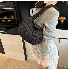 Elegante bolso de hombro acolchado negro llevado por modelo en una cocina acogedora
