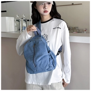 Détail d'un sac bandoulière en jean bleu avec fermeture éclair porté par un mannequin
