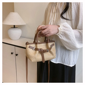 Detail of woven straw tote bag with brown leather trim and metallic buckle accents