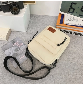 Detail of canvas crossbody bag with flip pocket and brown logo patch on desk