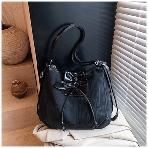 Detailed shot of black tote bag with bow drawstring and metal buckles on beige fabric