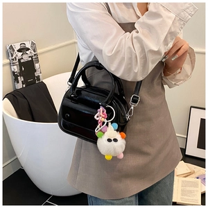 Detail of black patent leather crossbody bag with a white fluffy monster charm
