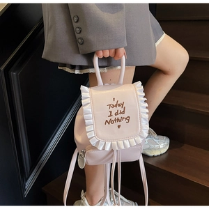 Close-up of pink mini backpack featuring white ruffle trim and embroidered quote detail