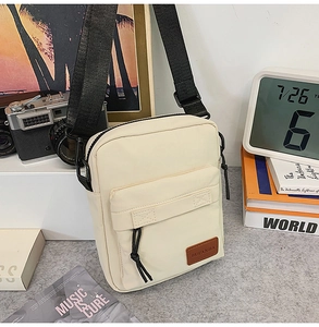 Detail of beige nylon crossbody bag with wide black strap and leather logo patch