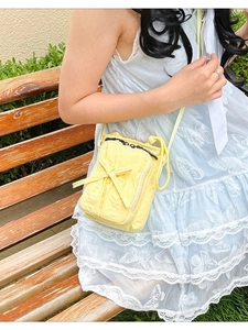 Pale yellow quilted crossbody bag with decorative bow and black zipper on park bench
