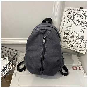 Détail d'un sac à dos en denim noir délavé avec poche zippée verticale et poignée
