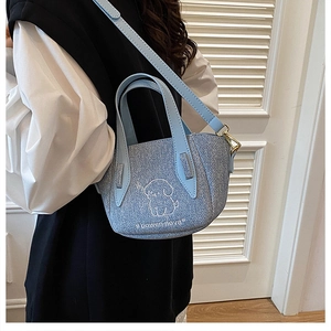 Close-up of light blue denim tote with white dog embroidery and bowen nova text logo