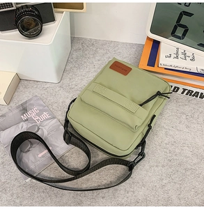 Still life view of green nylon crossbody bag with leather patch on gray felt surface
