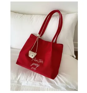 Detail of red canvas tote bag with white embroidery and beige mini pouch charm