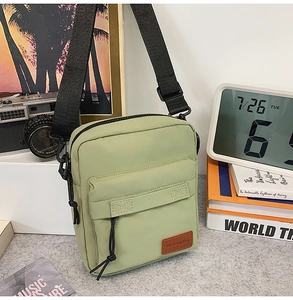 Detail view of a light green canvas crossbody bag with brown leather tag and black strap