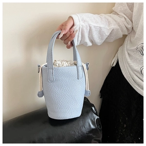 Close-up of light blue bucket bag in lychee leather with drawstring closure and top handles