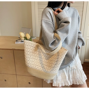 Détail de dentelle blanche superposée sur un sac cabas en paille porté par un mannequin