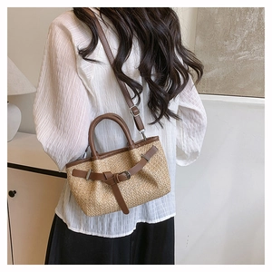 Detail of hand-woven straw crossbody bag with brown leather trim and metal buckles