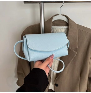 Détail d'un petit sac bleu clair porté à la main, montrant la texture cuir grainé lychee
