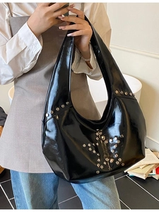 Glossy black punk hobo bag with silver star rivets shown in a stylish indoor setting