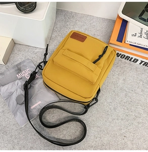 Top-down view of yellow nylon crossbody phone bag with black strap and leather label