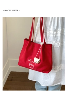 Detailed shot of red canvas tote bag with embroidered white lettering and logo charm