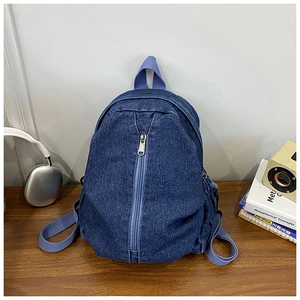 Détail d'un sac à dos en jean bleu avec poche à fermeture éclair métallique verticale
