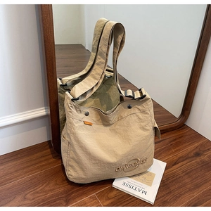 Dettaglio borsa tote in tela beige con tracolla regolabile su pavimento in legno