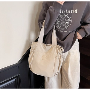 Close-up of beige nylon tote bag with wide shoulder strap and elastic side pockets
