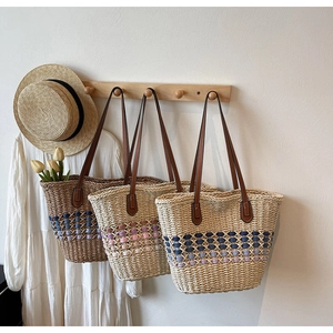 Trois sacs cabas en paille tressée marron et beige avec pompons colorés sur crochets