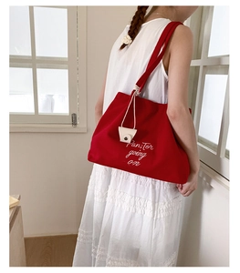 Detail of red canvas tote bag with white lettering and beige accessory charm