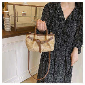 Detail of hand-woven straw crossbody bag with brown leather trim and decorative buckle